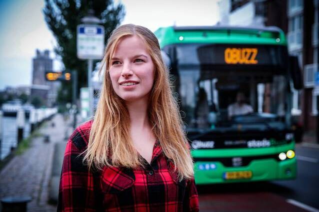 Een blonde vrouw staat voor een bus van Qbuzz