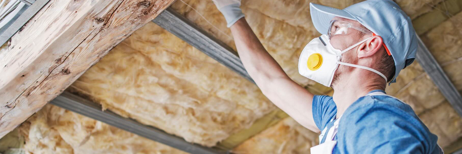 Man met luchtmasker werkt aan dakisolatie in woning.