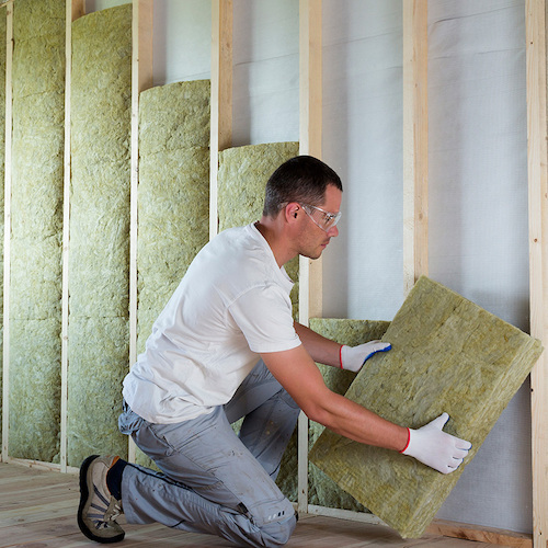 Man met werkbril en handschoenen plaatst isolatiemateriaal in muur